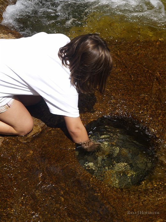 _8054545.JPG - Jillian explores a small pothole in the granite.  Eddying water spins pebbles and rocks in circles.  The spinning rocks gradually erodes the granite until depressions form.  Over time these potholes can get quite large by adding more and more stones to the mix.