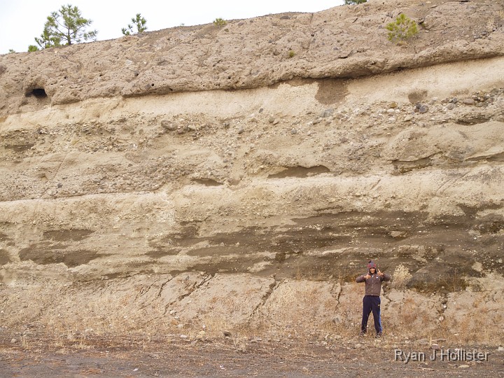 _B085505.JPG - Nav gives some great scale to an interesting road-cut in Cold Springs.  Notice all the sedimentary layers?  The layer in the middle is a nice rounded conglomerate of an old stream bed, followed by some more fine sediments of volcanic ash, topped by a lahar of breccia.  Cool!